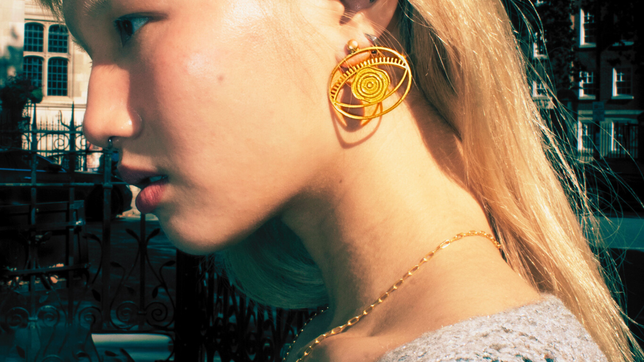 Editorial close-up of model wearing gold evil eye statement earrings and chain necklace by Jéy Jewels by Divya