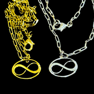 Two necklaces with infinity pendants, one gold and one silver, on a black background by Jéy Jewels by Divya